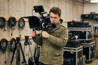 Jeune homme en formation audiovisuelle tenant une caméra professionnelle dans un atelier de cinéma sans diplôme de bac